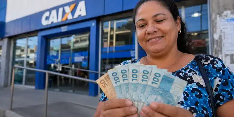 Mulher segura cédulas de real em frente a uma agência da Caixa, representando a solicitação do Saque Calamidade do FGTS até 29 de julho de 2026.