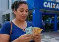 Mulher conta cédulas em frente a uma agência da Caixa, representando o pagamento de até R$ 1.050 do Bolsa Família.
