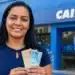Mulher segura cédulas em frente a uma agência da Caixa, representando os pagamentos de até R$ 800 do Bolsa Família nos dias 23 e 24 de julho.