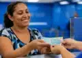 Mulher recebendo dinheiro referente ao benefício Mães de Pernambuco, representando o pagamento de R$ 1.500 em 2026.