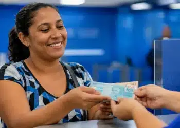 Mulher recebendo dinheiro referente ao benefício Mães de Pernambuco, representando o pagamento de R$ 1.500 em 2026.