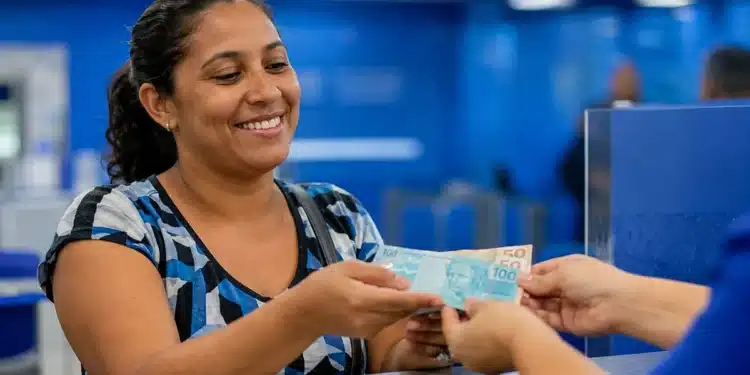 Mulher recebendo dinheiro referente ao benefício Mães de Pernambuco, representando o pagamento de R$ 1.500 em 2026.