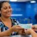 Mulher recebendo dinheiro referente ao benefício Mães de Pernambuco, representando o pagamento de R$ 1.500 em 2026.