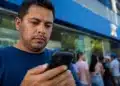 Trabalhador consulta pelo celular, em frente a uma agência da Caixa, informações sobre o saque-aniversário do FGTS, disponível até 31 de julho.