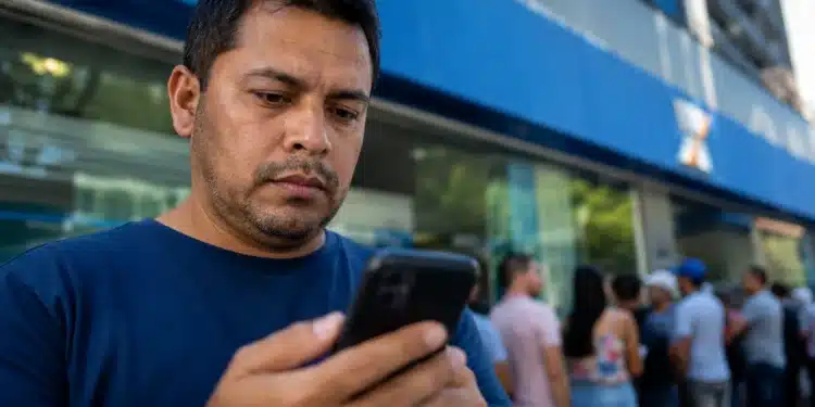 Trabalhador consulta pelo celular, em frente a uma agência da Caixa, informações sobre o saque-aniversário do FGTS, disponível até 31 de julho.