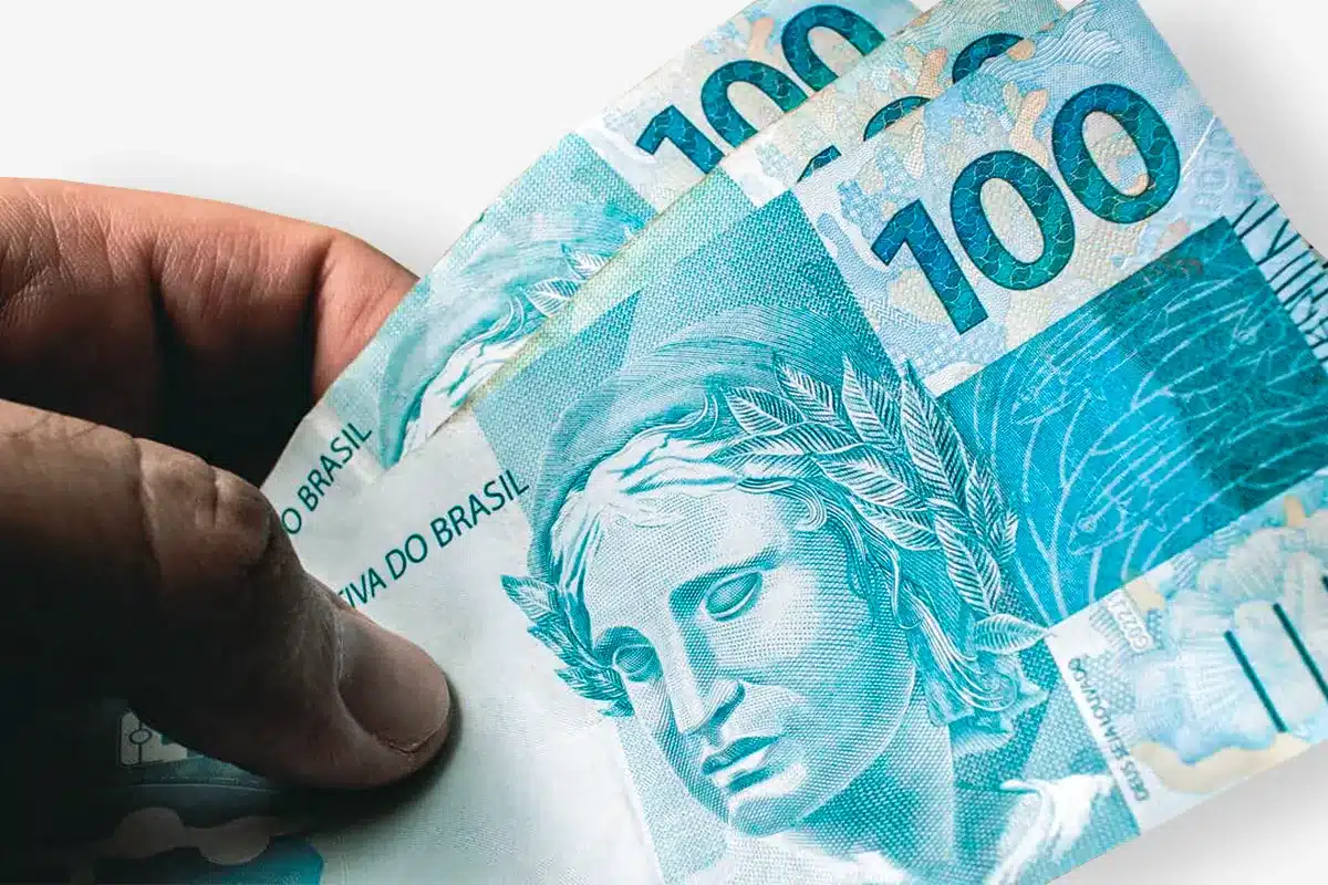 Mães de Pernambuco - Critérios de recebimento Mão segurando três notas de R$ 100, representando os critérios para receber o benefício do Mães de Pernambuco.