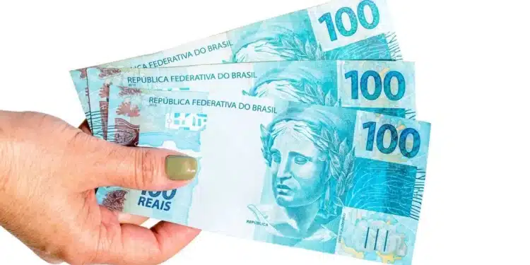 Mão segurando três notas de R$ 100 para representar o pagamento de agosto do Mães de Pernambuco