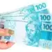 Mão segurando três notas de R$ 100 para representar o pagamento de agosto do Mães de Pernambuco