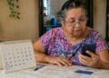 Beneficiária idosa consulta o celular ao lado de um calendário de mesa com o dia 27 circulado, data em que começa o pagamento do BPC de julho