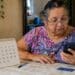 Beneficiária idosa consulta o celular ao lado de um calendário de mesa com o dia 27 circulado, data em que começa o pagamento do BPC de julho