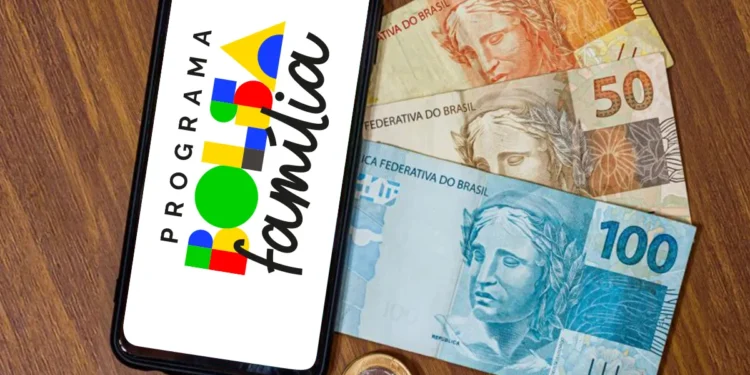 Celular com símbolo do Bolsa Família ao lado de cédulas de real representa os pagamentos do benefício em agosto de 2026.