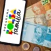 Celular com símbolo do Bolsa Família ao lado de cédulas de real representa os pagamentos do benefício em agosto de 2026.