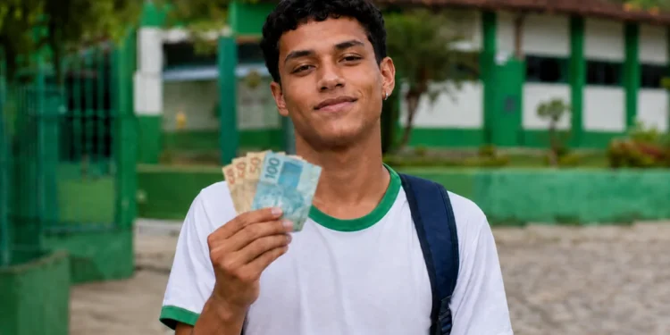 Estudante segura cédulas de dinheiro em frente à escola, representando o calendário de pagamentos do Pé-de-Meia de setembro.