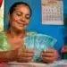 Beneficiária do programa Mães de Pernambuco segura notas de dinheiro em casa, representando o pagamento de R$ 300 em agosto.