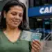 Beneficiária do Bolsa Família segura nota de R$ 100 em frente a uma agência da Caixa.