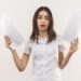 young girl in white shirt holding blank pages looking at camera confused standing over white background