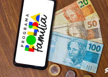 Celular exibindo o logo do programa Bolsa Família, com notas de 20, 50 e 100 reais e moedas ao fundo