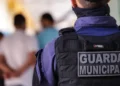 Agente da Guarda Municipal de costas, com uniforme e colete tático, durante evento público.