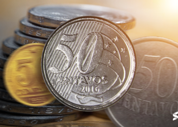 Moeda de 50 centavos destacada, com outras moedas ao fundo, representando um exemplar raro com erro de cunho quebrado.