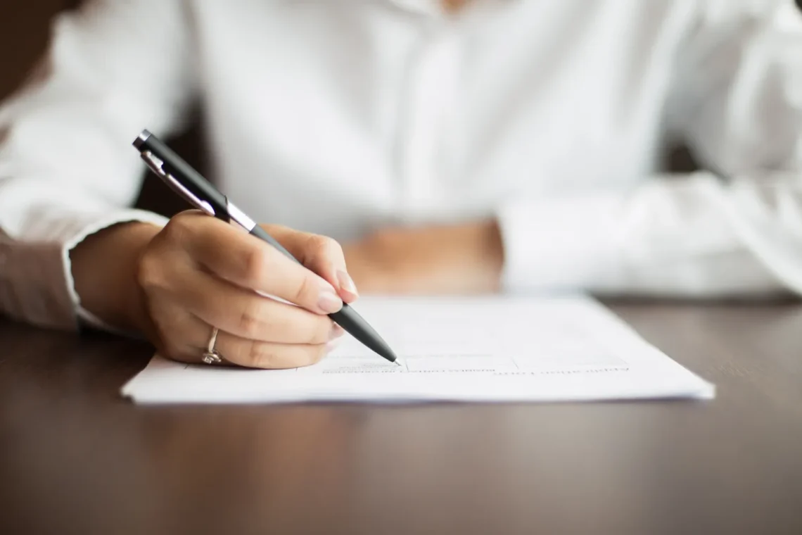 Mão feminina assinando um documento, representando a preparação para o Concurso CNEN