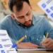 Homem escrevendo em um caderno enquanto preenche um formulário