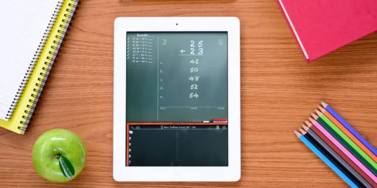 Tablet com aplicativo de matemática exibindo cálculos, rodeado por materiais escolares