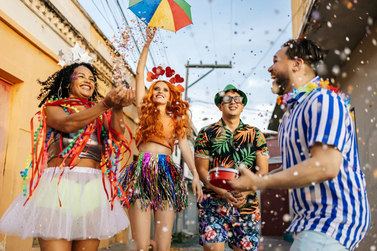 Grupo de pessoas fantasiadas se divertindo no Carnaval, jogando confete e comemorando na rua