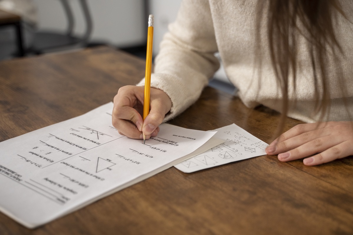 Pessoa resolvendo prova de matemática com lápis sobre mesa de madeira.