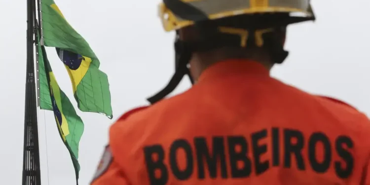 Bombeiro de costas observando as bandeiras do Brasil, representando o concurso Bombeiros DF em andamento.