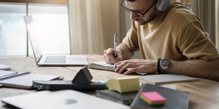 Homem estudando com fones de ouvido e fazendo anotações para concursos públicos.