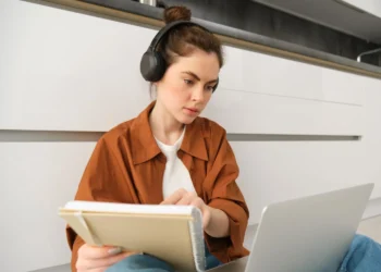 Mulher estudando com fones de ouvido e notebook, utilizando tecnologia para otimizar o aprendizado