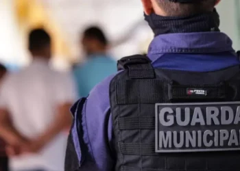 Guarda Municipal de costas, vestindo uniforme e colete tático com a inscrição "Guarda Municipal"