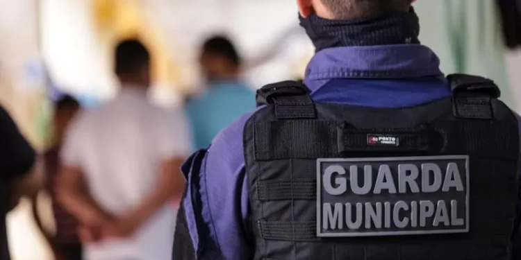 Guarda Municipal de costas, vestindo uniforme e colete tático com a inscrição "Guarda Municipal"