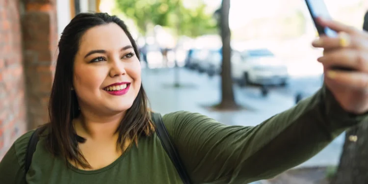 Mulher sorrindo e tirando uma selfie, representando o alerta sobre o golpe da selfie