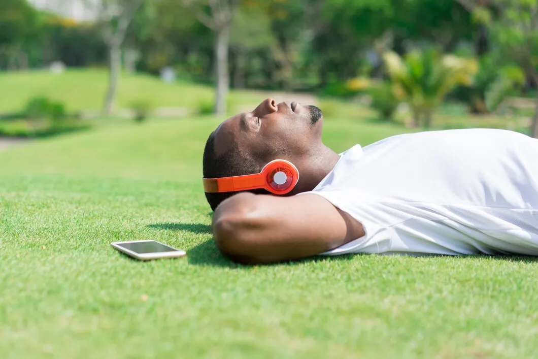 Pessoa relaxando no gramado com fones de ouvido, representando a importância do descanso e lazer para manter a produtividade.