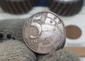 Moeda rara de 5 centavos do ano 2000 sendo segurada com luvas, destacando detalhes e relevos.