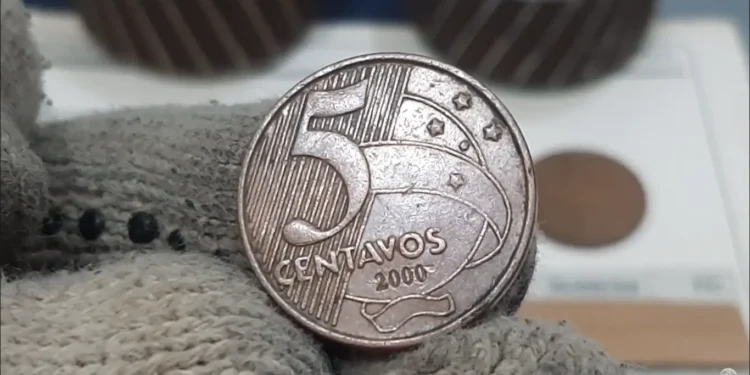 Moeda rara de 5 centavos do ano 2000 sendo segurada com luvas, destacando detalhes e relevos.