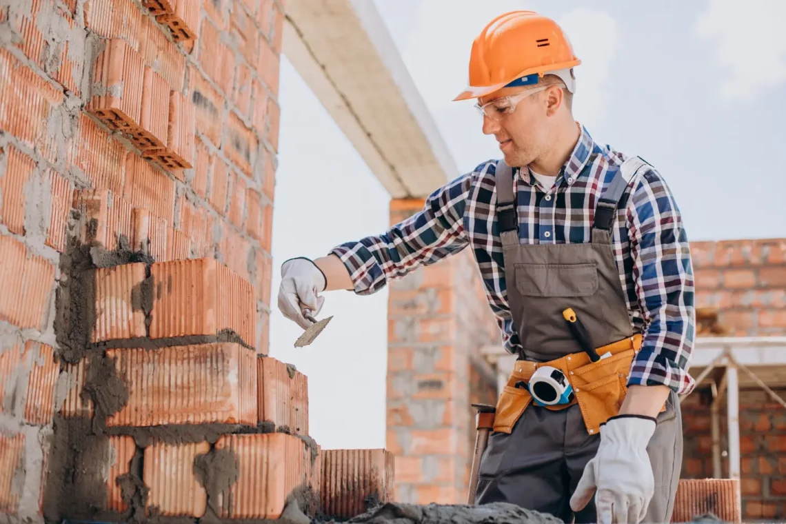 Pedreiro aplicando cimento e assentando tijolos em obra de construção civil