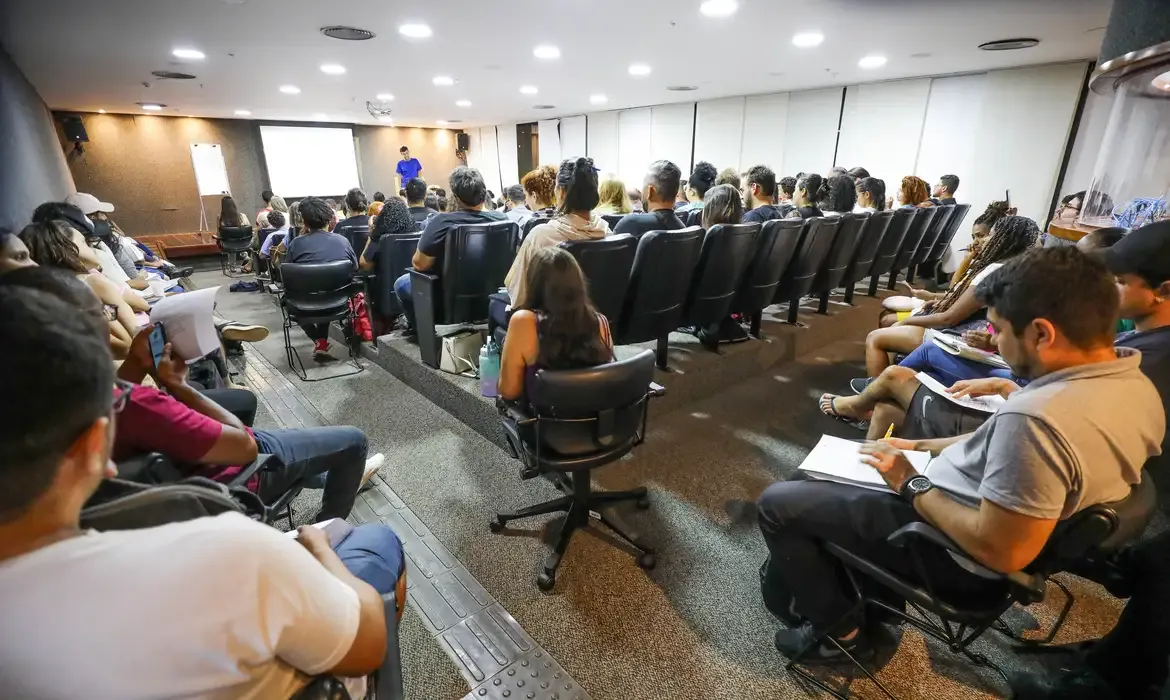 Sala de aula com candidatos assistindo a uma palestra preparatória para concurso público.