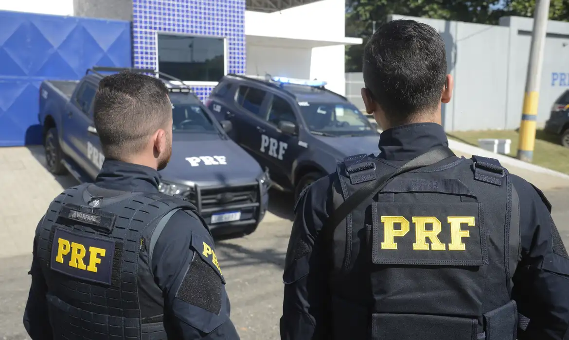 Policial Rodoviário Federal de costas, com viaturas ao fundo, representando os requisitos para o cargo de PRF.