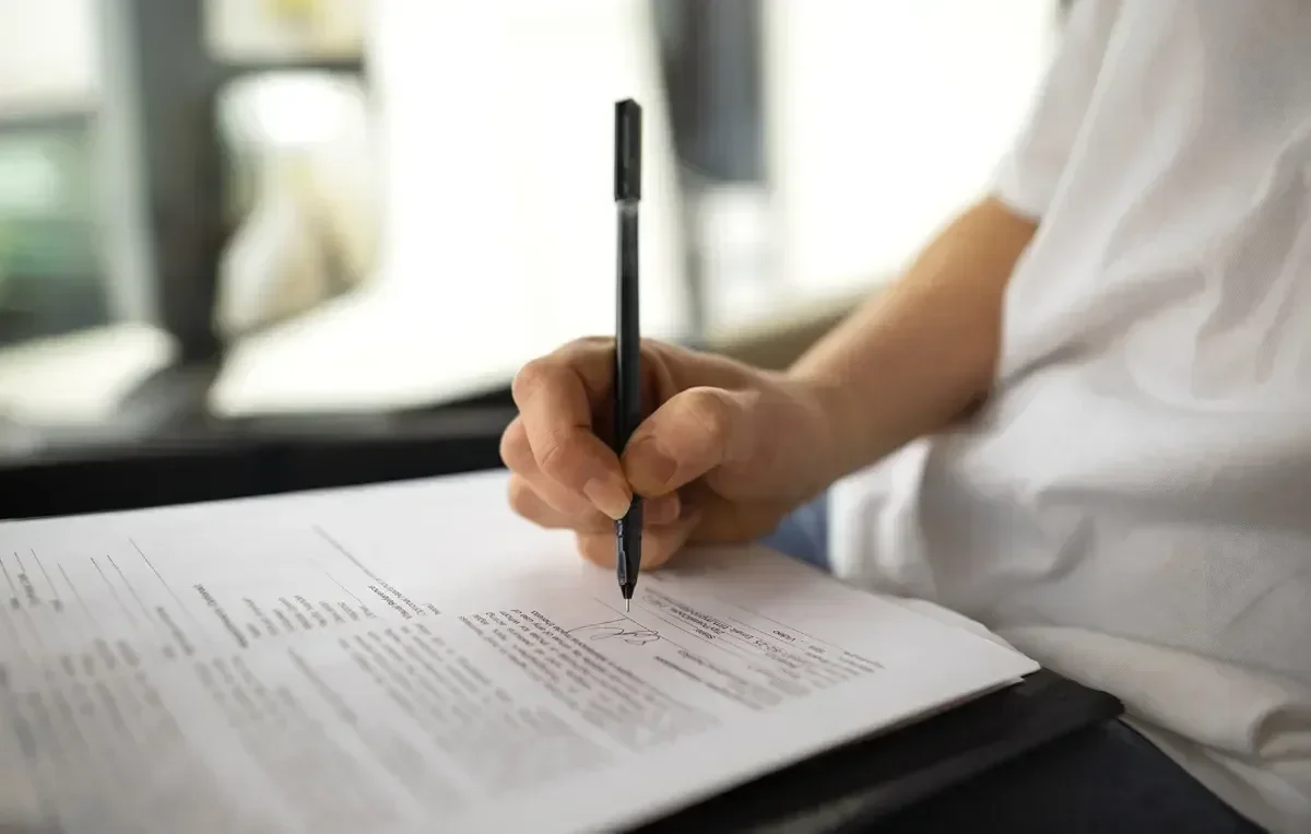  Pessoa assinando um documento, representando o processo de inscrição e requisitos do concurso da Polícia Penal PB.