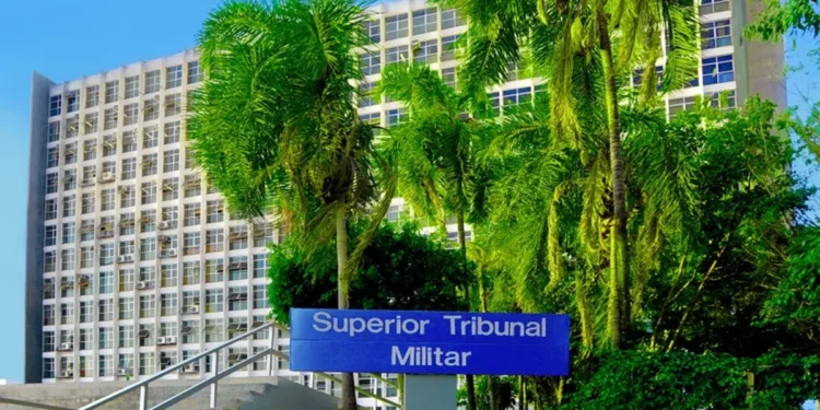 Fachada do Superior Tribunal Militar com placa identificativa, cercada por palmeiras e vegetação, destacando a sede do órgão