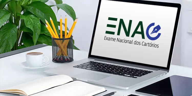 Notebook exibindo a logo do Exame Nacional dos Cartórios (ENAC) sobre uma mesa com materiais de estudo