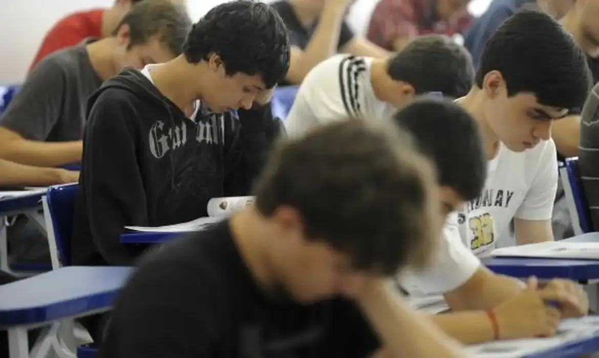 Grupo de candidatos concentrados realizando uma prova em sala de aula.