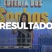 Mulher exibindo o resultado da Loteria dos Sonhos ao vivo, com bolas e sorteio