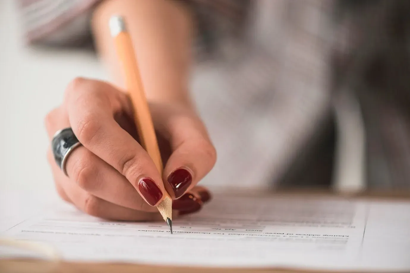 Candidata preenchendo um formulário de inscrição com lápis sobre uma mesa.