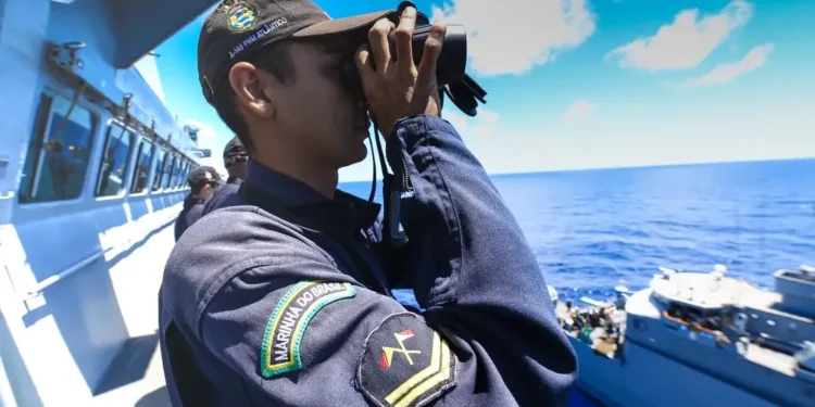 Militar da Marinha do Brasil observando o mar com binóculos em uma embarcação.