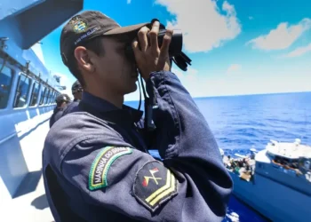 Militar da Marinha do Brasil observando o mar com binóculos a bordo de um navio.