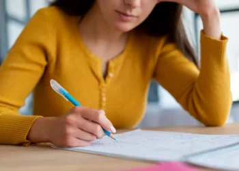 Pessoa estudando concentrada, escrevendo em um caderno com lápis azul, representando preparação para concursos.