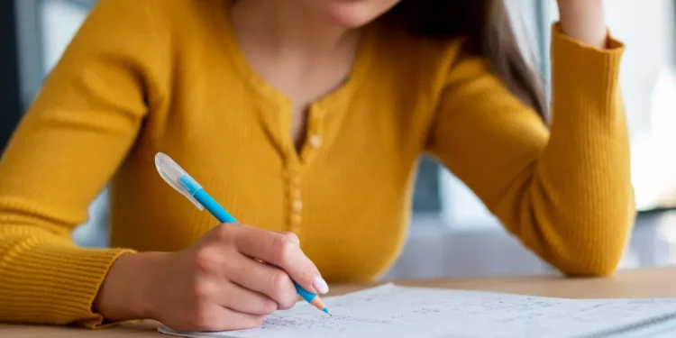 Pessoa estudando concentrada, escrevendo em um caderno com lápis azul, representando preparação para concursos.